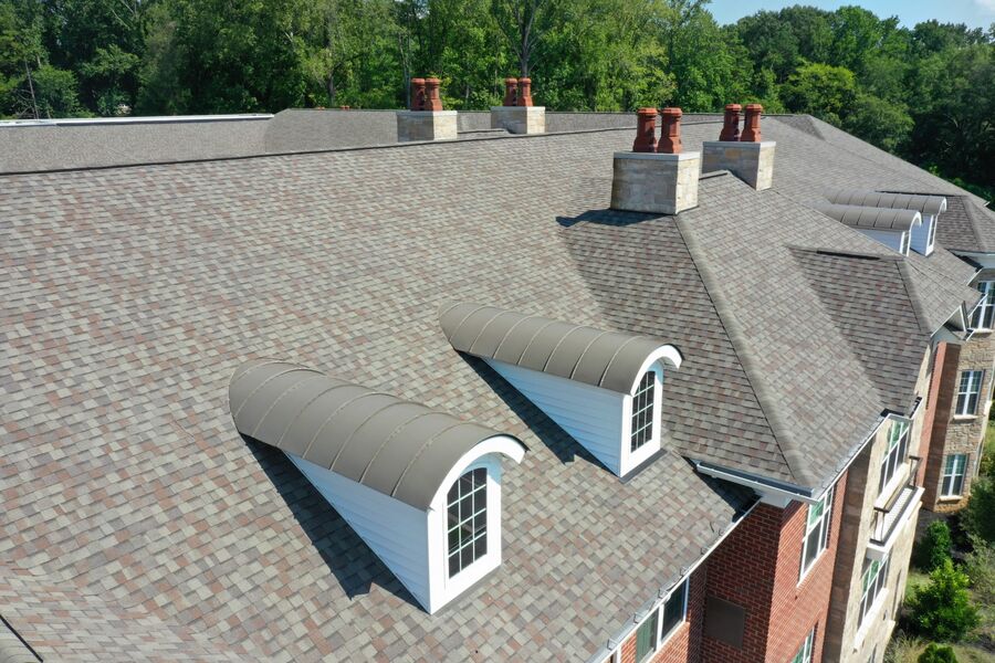 Aerial view of a large shingled residential roof with dormer windows and multiple chimneys