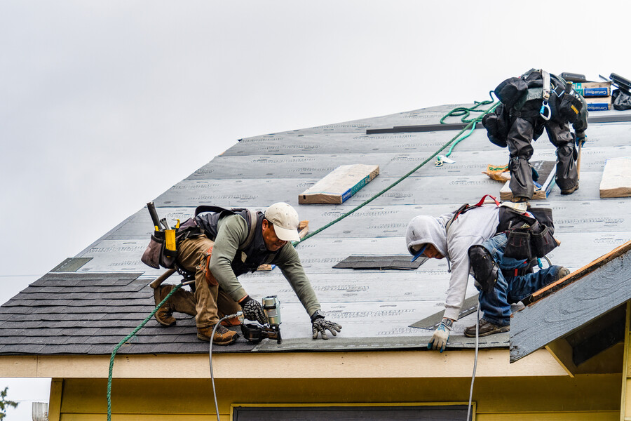 Roofing contractors installing new shingles on a house roof during replacement work