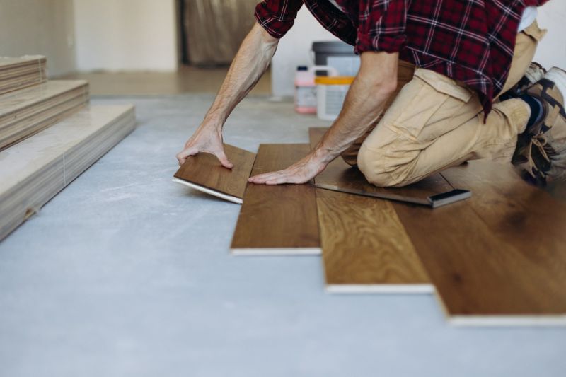 Floor installer kneeling and laying hardwood planks in a room during flooring installation